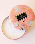A round tin 3 wick candle with an abstract floral and spotted design. The metal from the tin reflects light in a beautiful way, especially on its gold parts. The other colors on this tin are white and and a peach color.