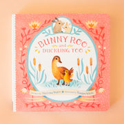 On a tan background is a pink book cover with an illustration of ducks and bunnies and the title that reads, "Bunny Roo and Duckling Too". 