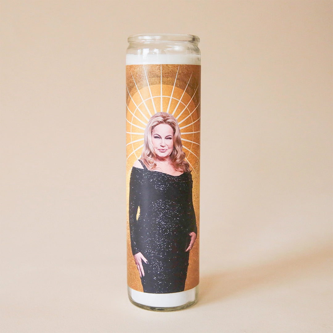 On a tan background is a prayer candle featuring a photo of Jennifer Coolidge on the front. 