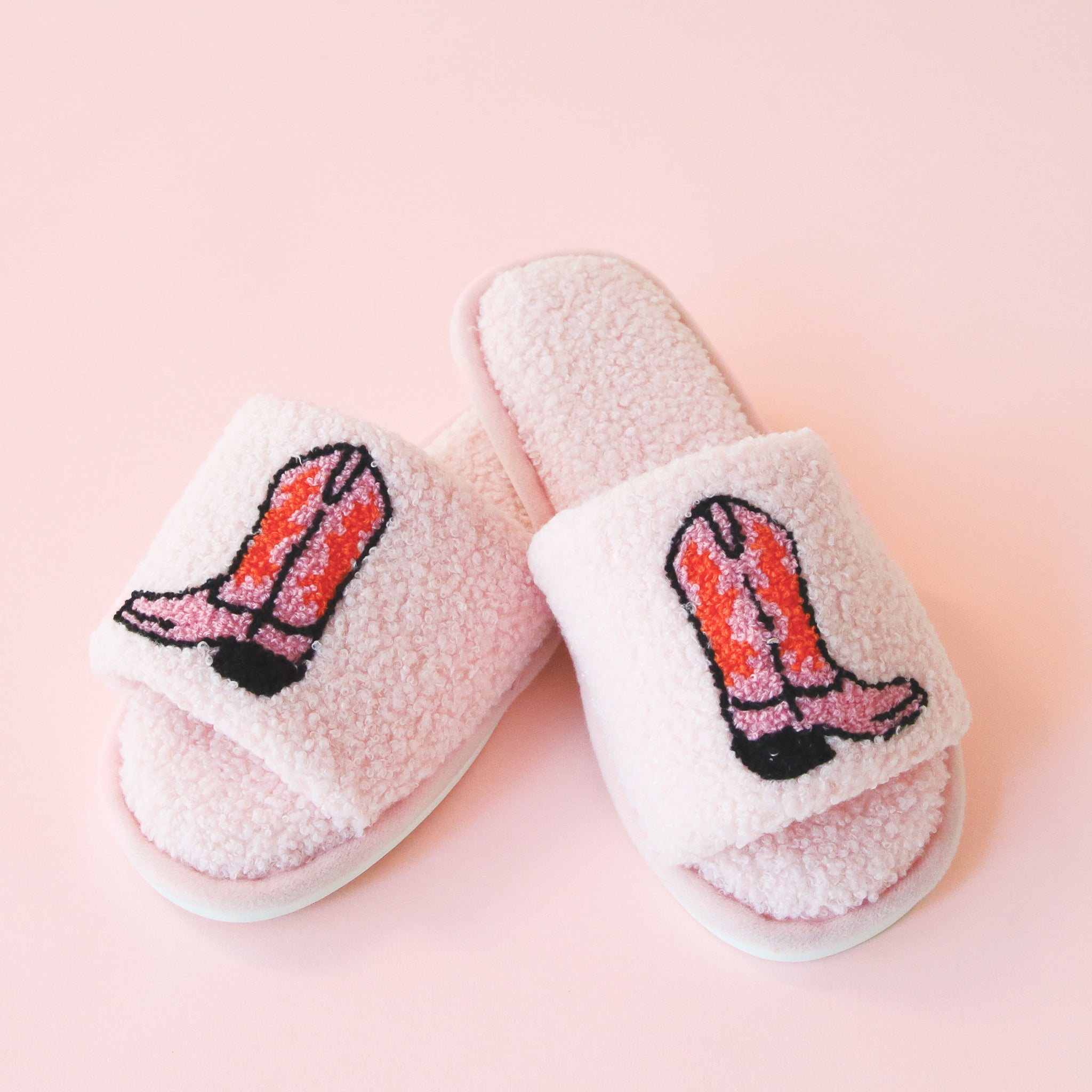 Pink fuzzy slide slippers with an open toe front and a pink and red cowgirl boot graphic on the top.