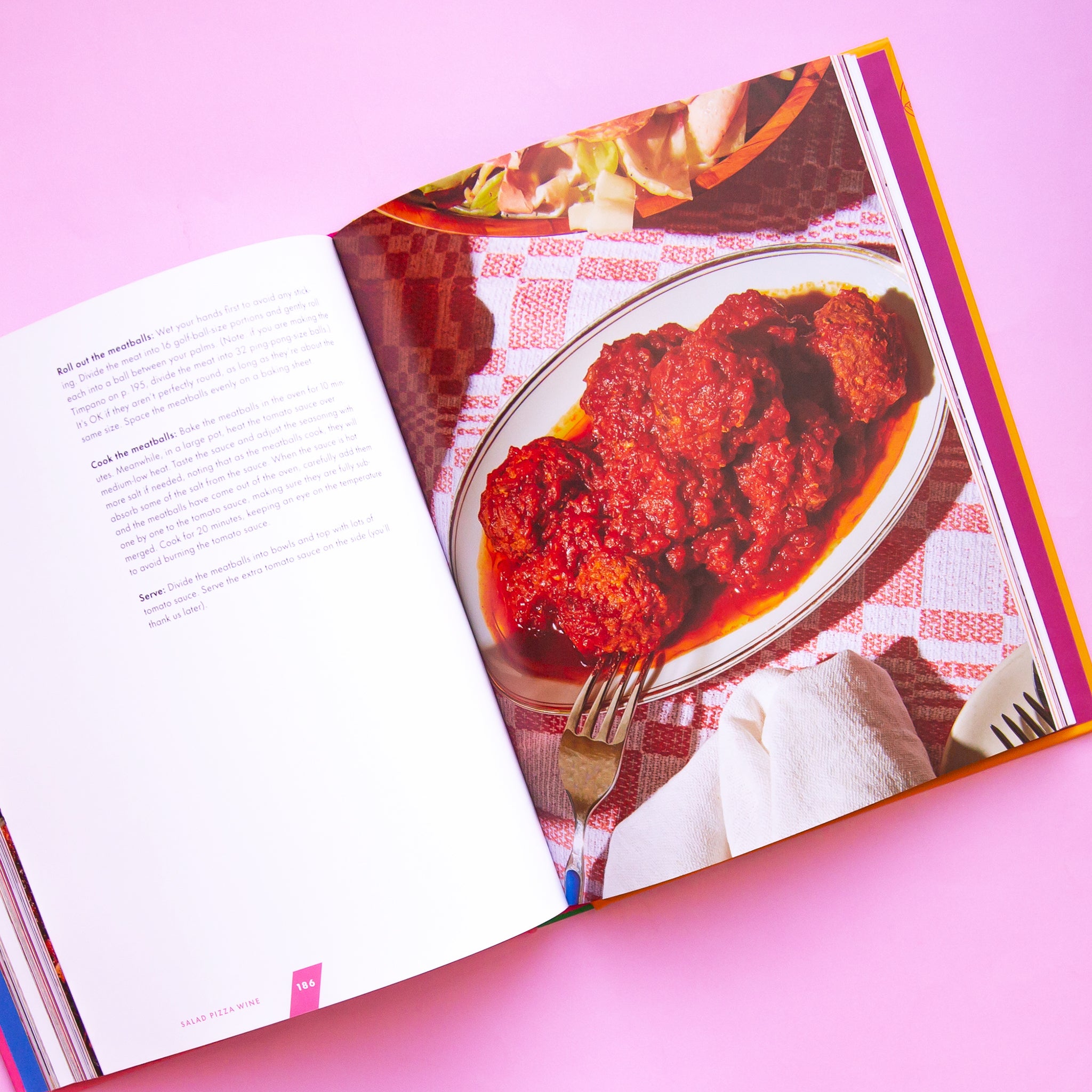 On a pink background is an opened up cook book with text on the left side and a photograph on the other. 