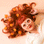 On a tan background is a white pair of flower shaped sunglasses with a light pink lens in the center.