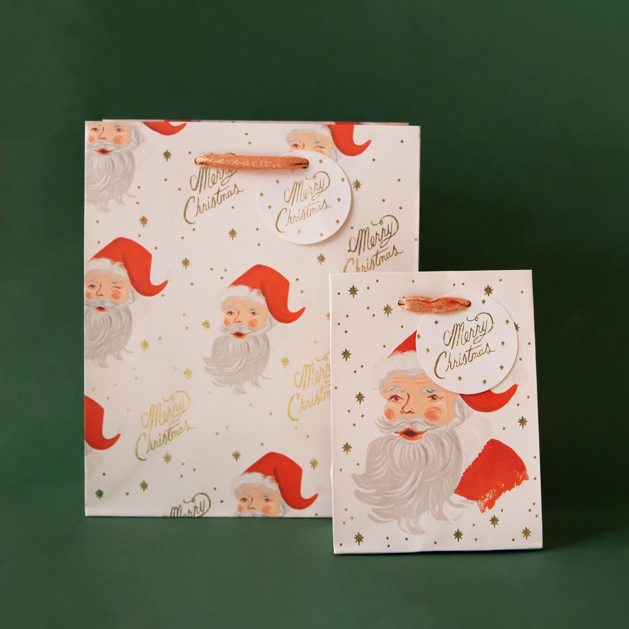 Two different sized ivory gift bags with a red Santa design along with gold text that reads, "Merry Christmas".