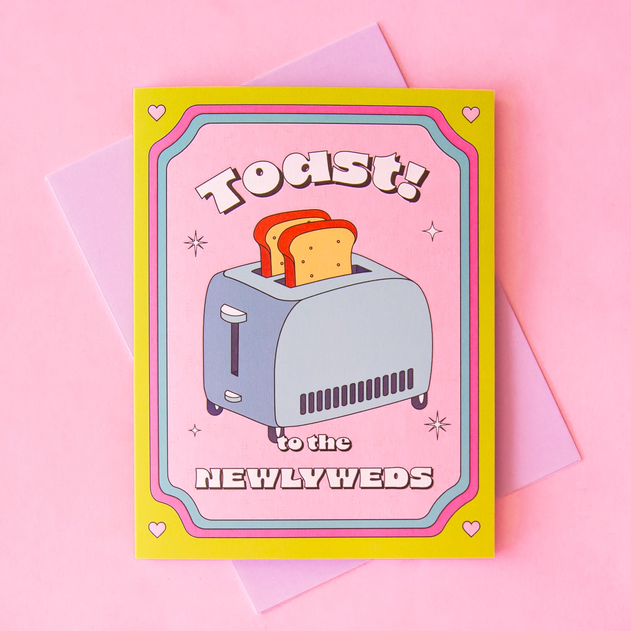 On a pink background is a multi colored card with a pink, yellow and blue border and a graphic of a toaster and toast coming out of it with text above and below that reads, &quot;Toast! to the Newlyweds&quot;. 