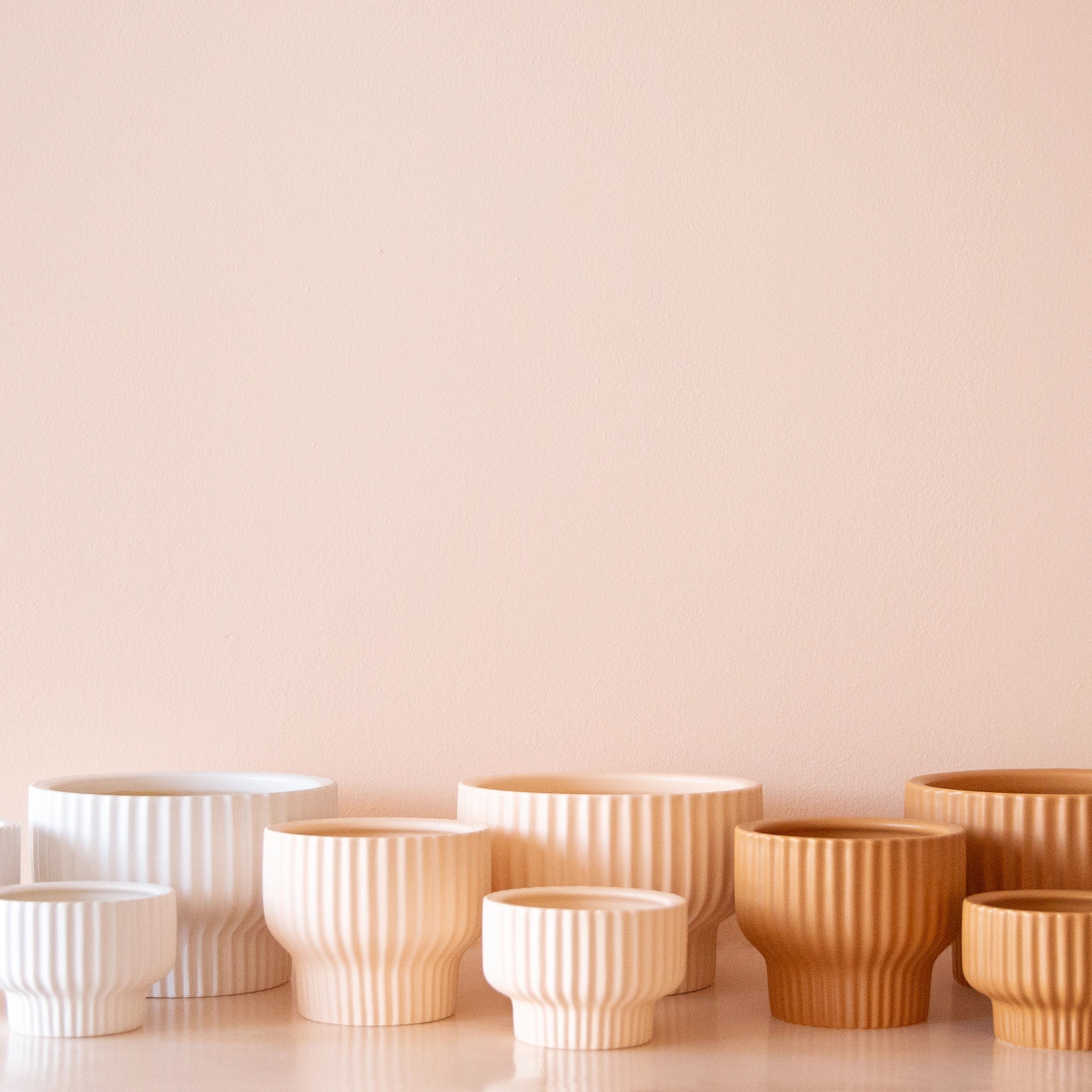 On a tan background is all three colors of the Presley Pedestal Pots. There is an ivory shade, ballerina, and ginger. 