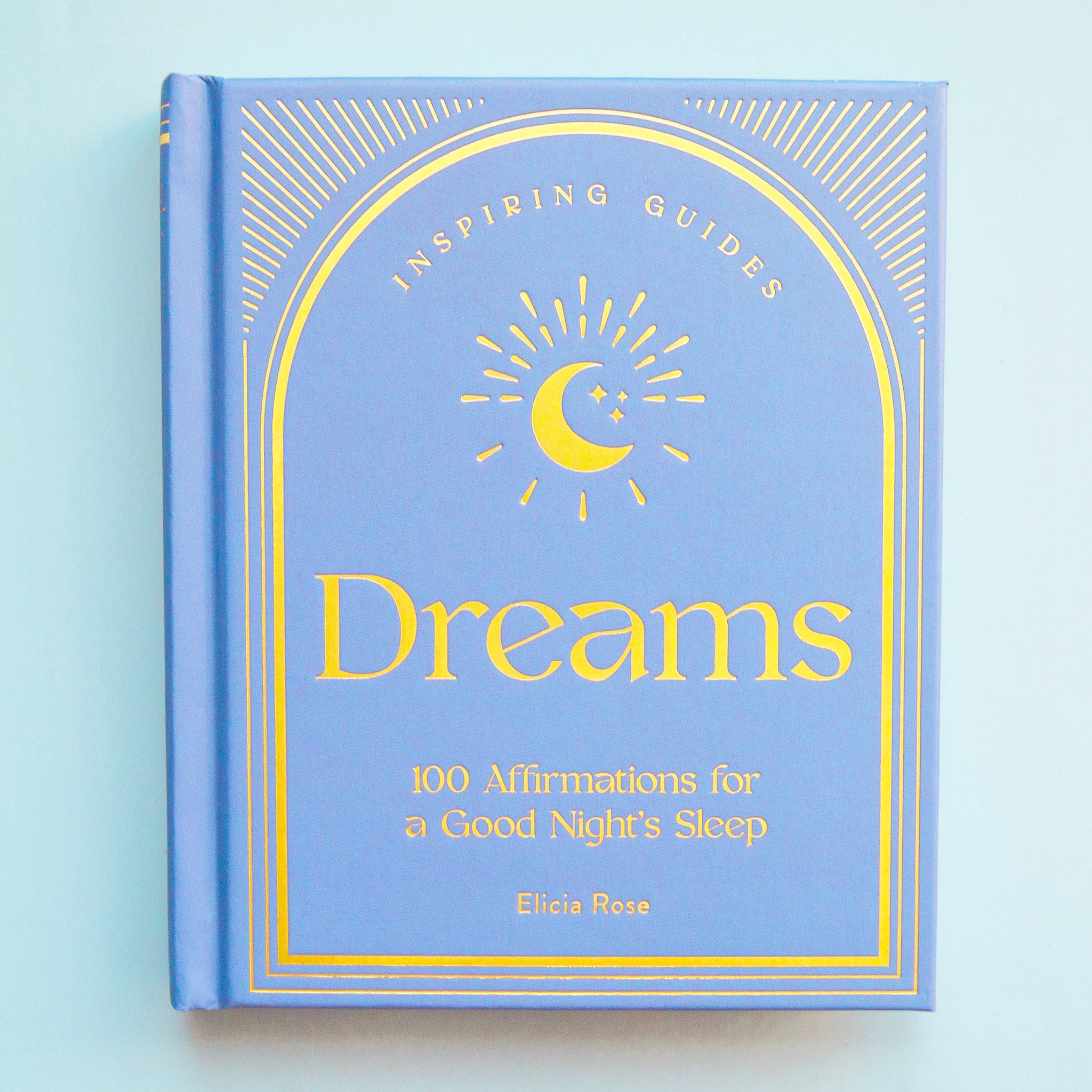On a blue background is a blue book with god text and moon design on the cover that reads, &quot;Inspiring Guides Dreams 100 Affirmations for a Good Night&#39;s Sleep&quot;. 