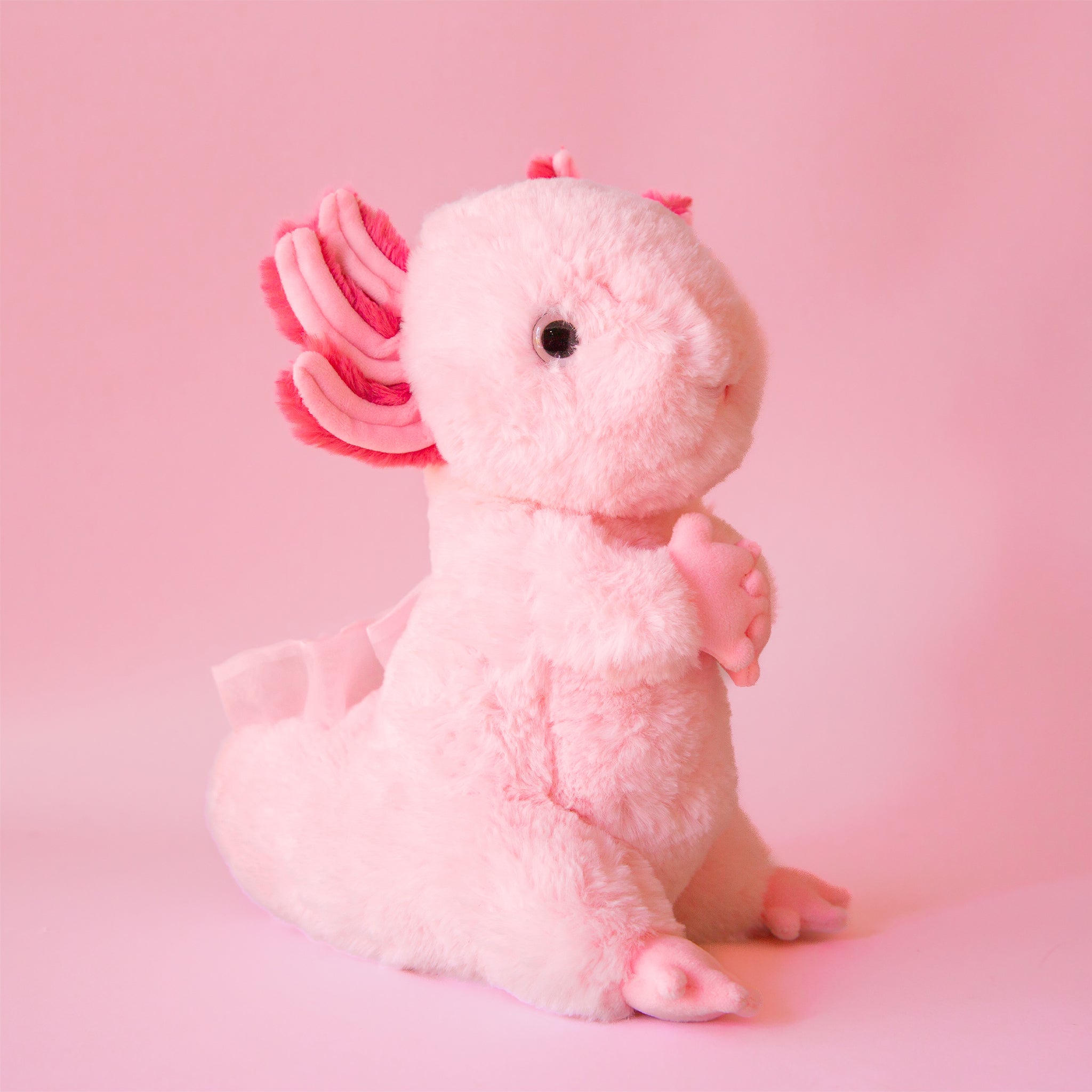 On a pink background is a light pink stuffed animal toy. 