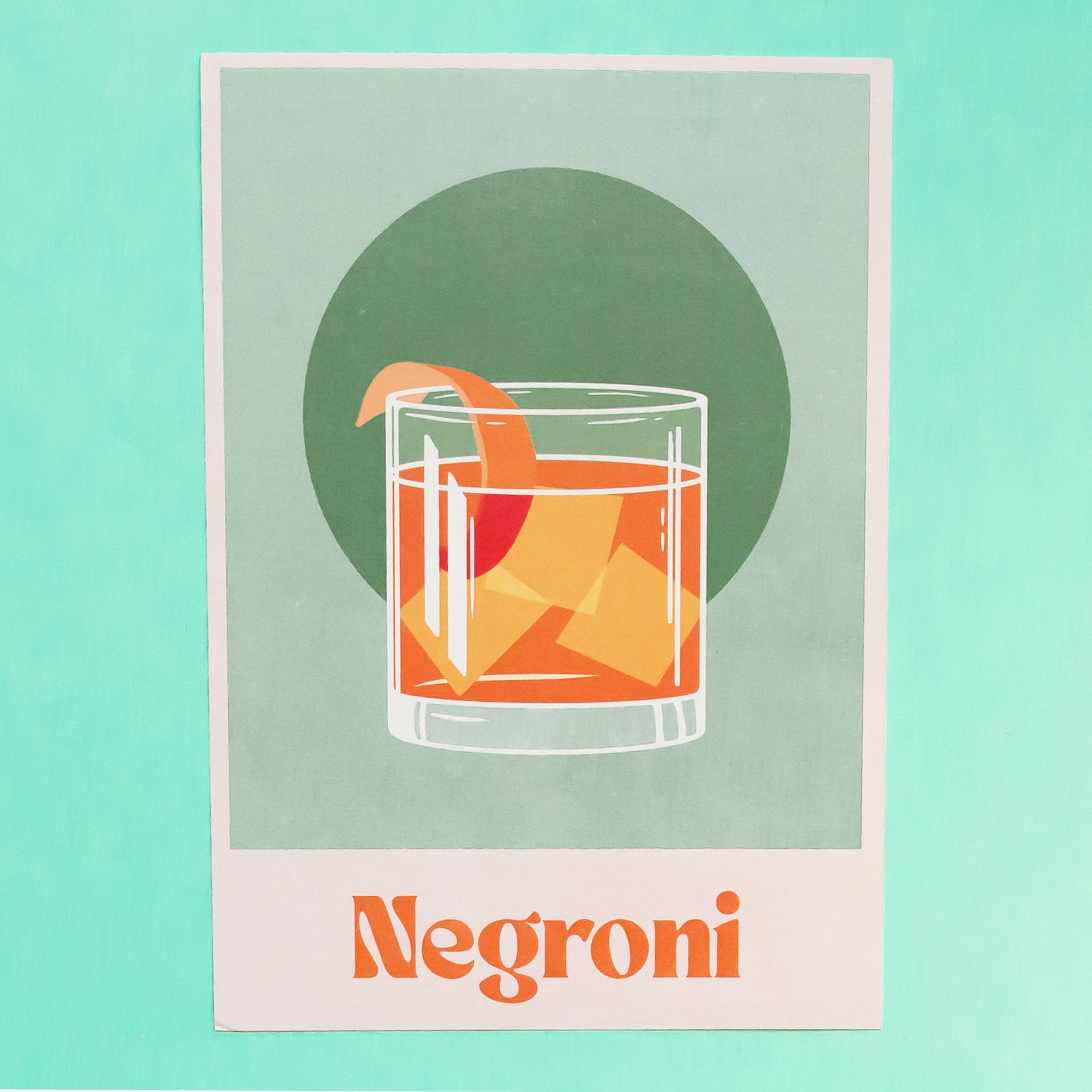 On a teal  background is a green art print with an off white border and orange text at the bottom that reads, "Negroni" as well as a graphic of a Negroni cocktail with an orange peel in the center.