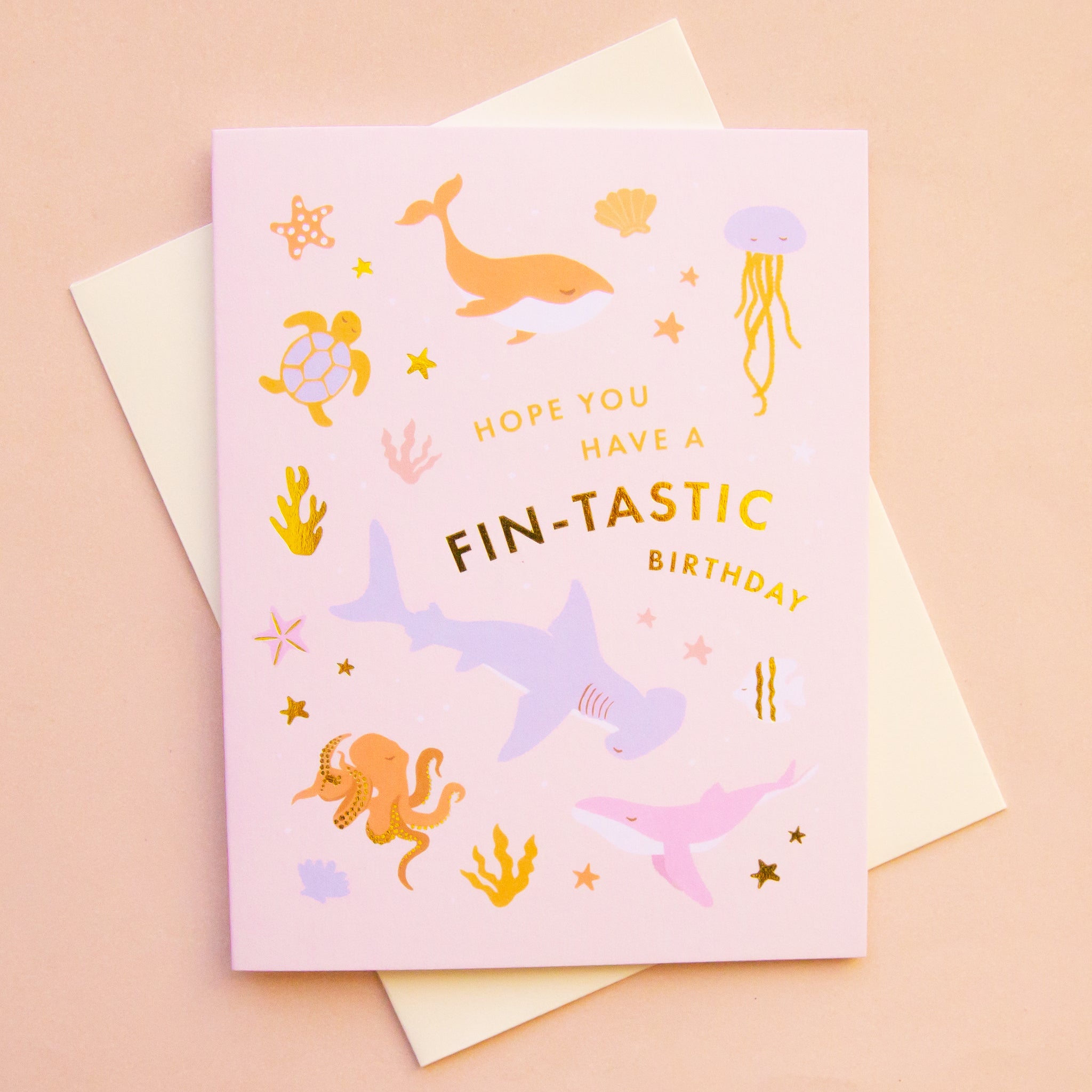 On a pink background is a pink card with ocean animals on it and text that reads, "Hope Your Have A Fin-Tastic Birthday".