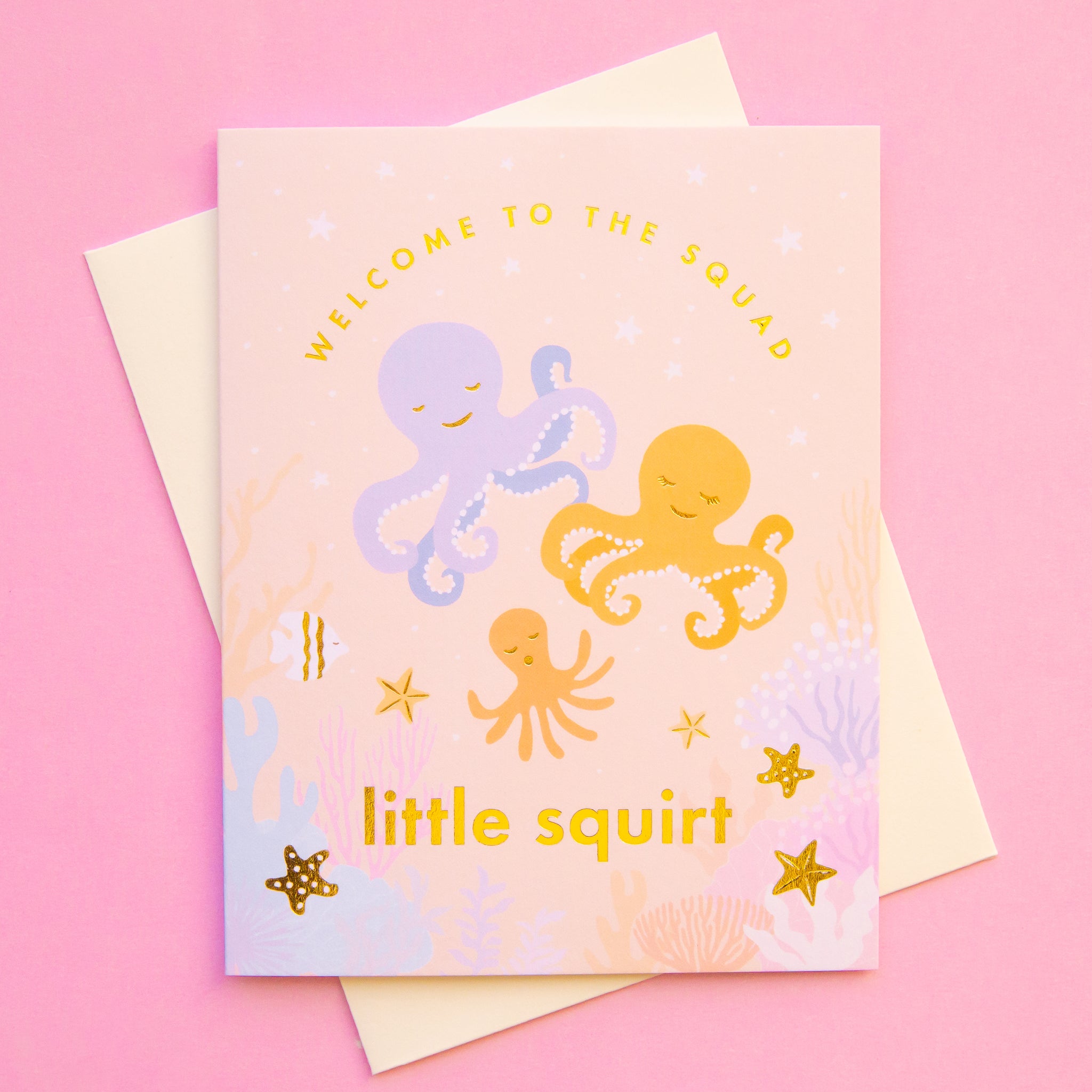On a pink background is a light pink ish orange card with three illustrations of octopus and gold text that reads, &quot;Welcome To The Squad little squirt&quot;.