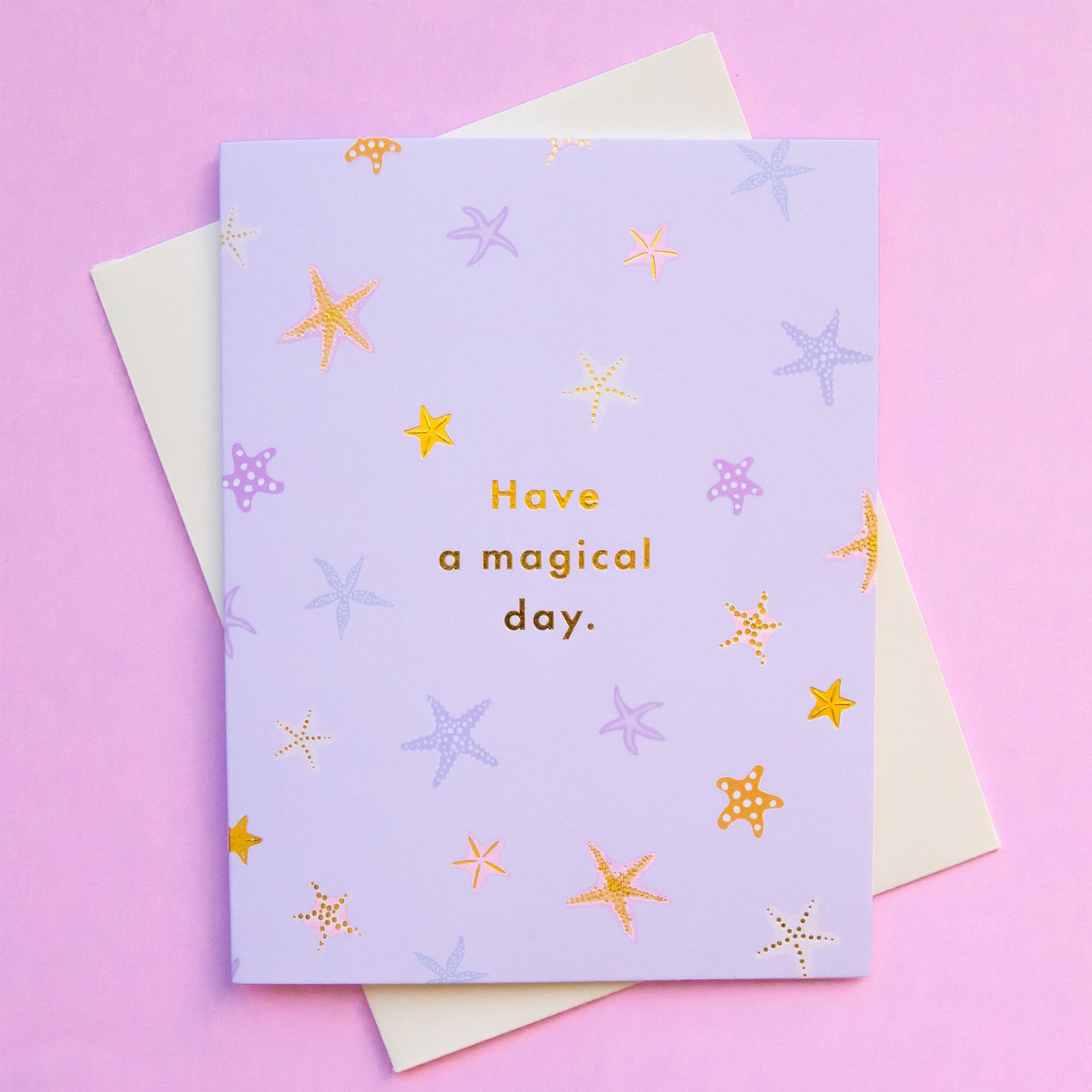 On a pink background is a light pink card with a multi colored starfish pattern and text in the center that reads, "Have a magical day.".