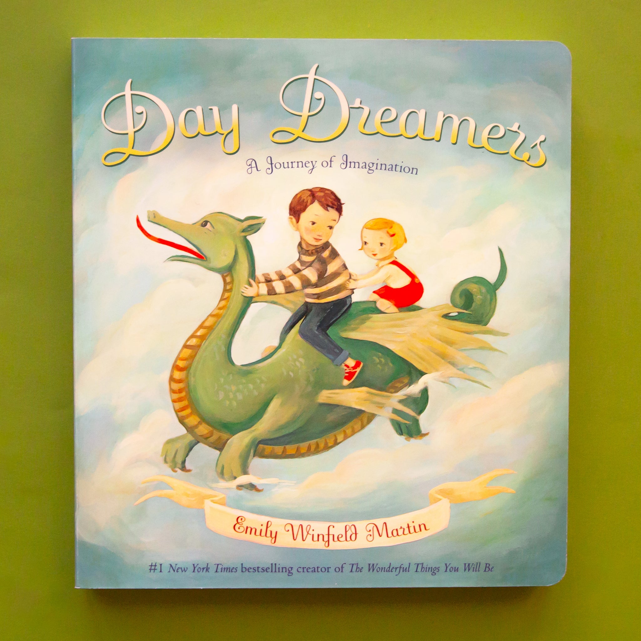 An aqua green book cover with the title, &quot;Day Dreamers: A Journey of Imagination&quot; along with an illustration of a dragon and two kids riding through the sky.