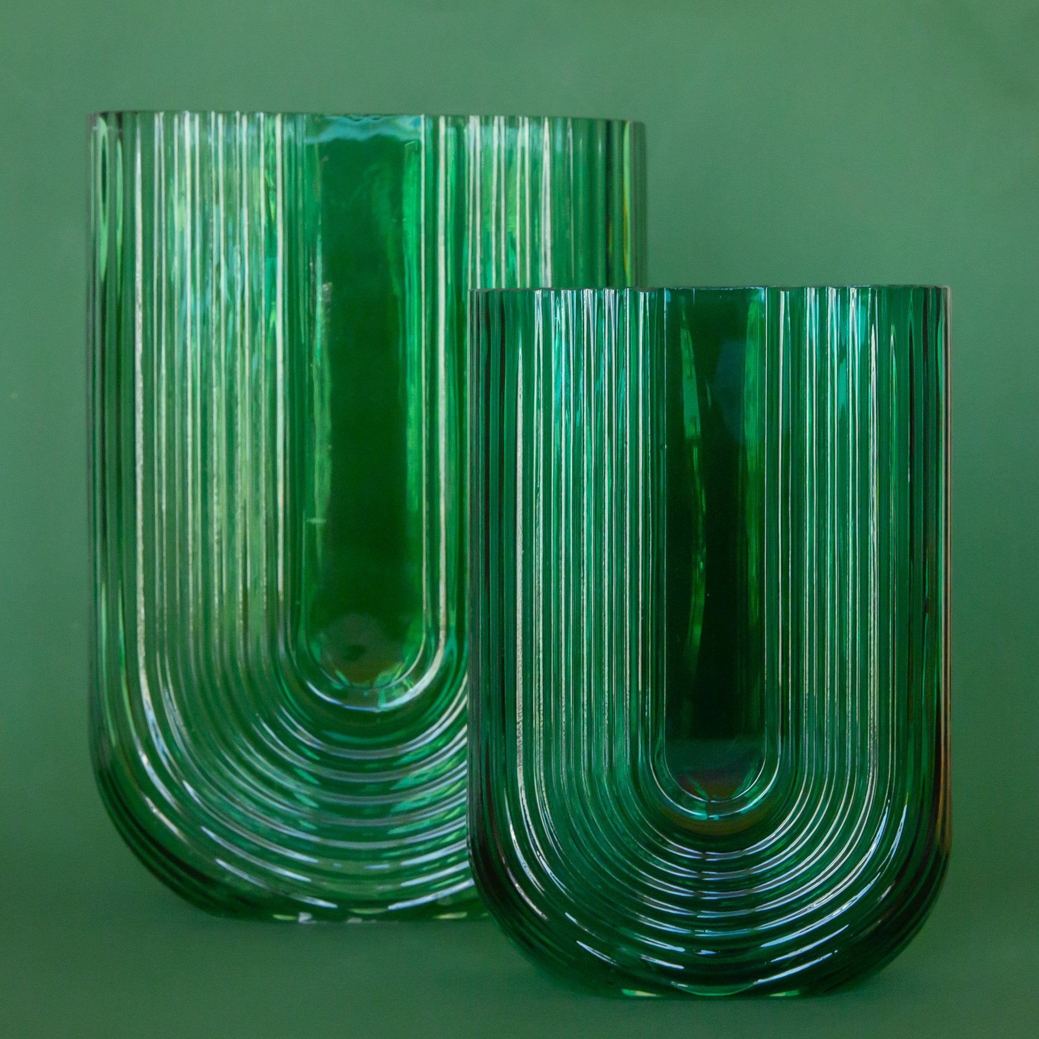 On a green background is two emerald green arched shaped glass vases. Each vase sold separately.