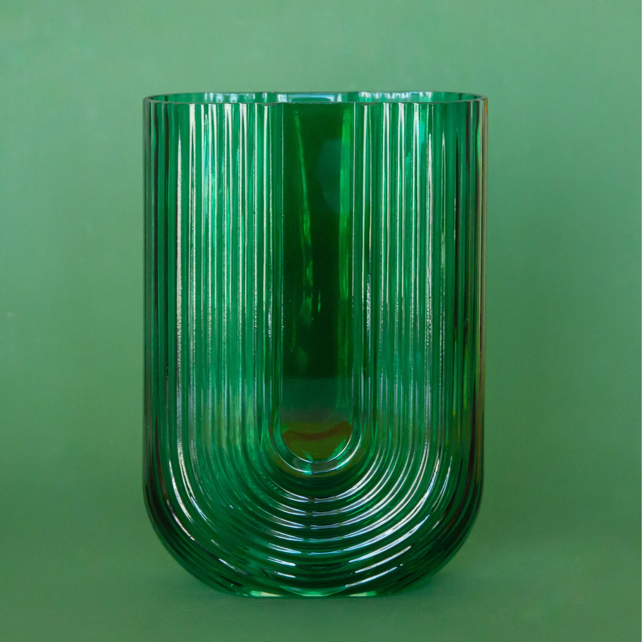 On a green background is an emerald green arched shaped glass vase. Each vase sold separately.
