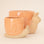 On a light peach background is two ceramic planters in the shape of a snail with a swirly light orange "shell". 