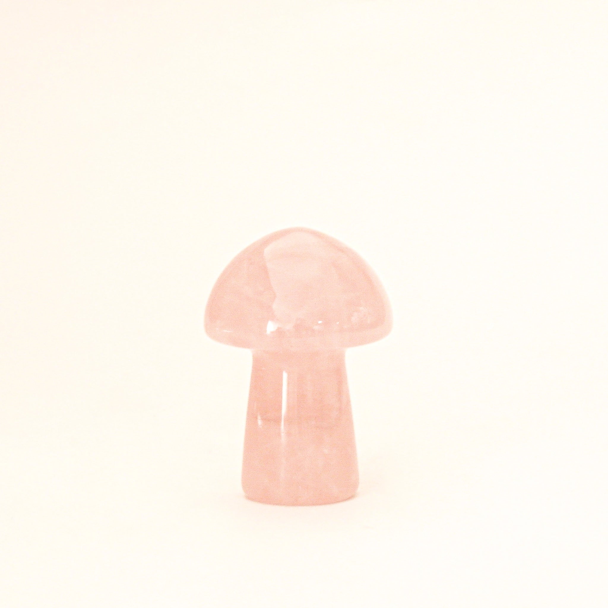 On a cream background is a model holding a tiny rose quartz crystal in the shape of a mushroom.