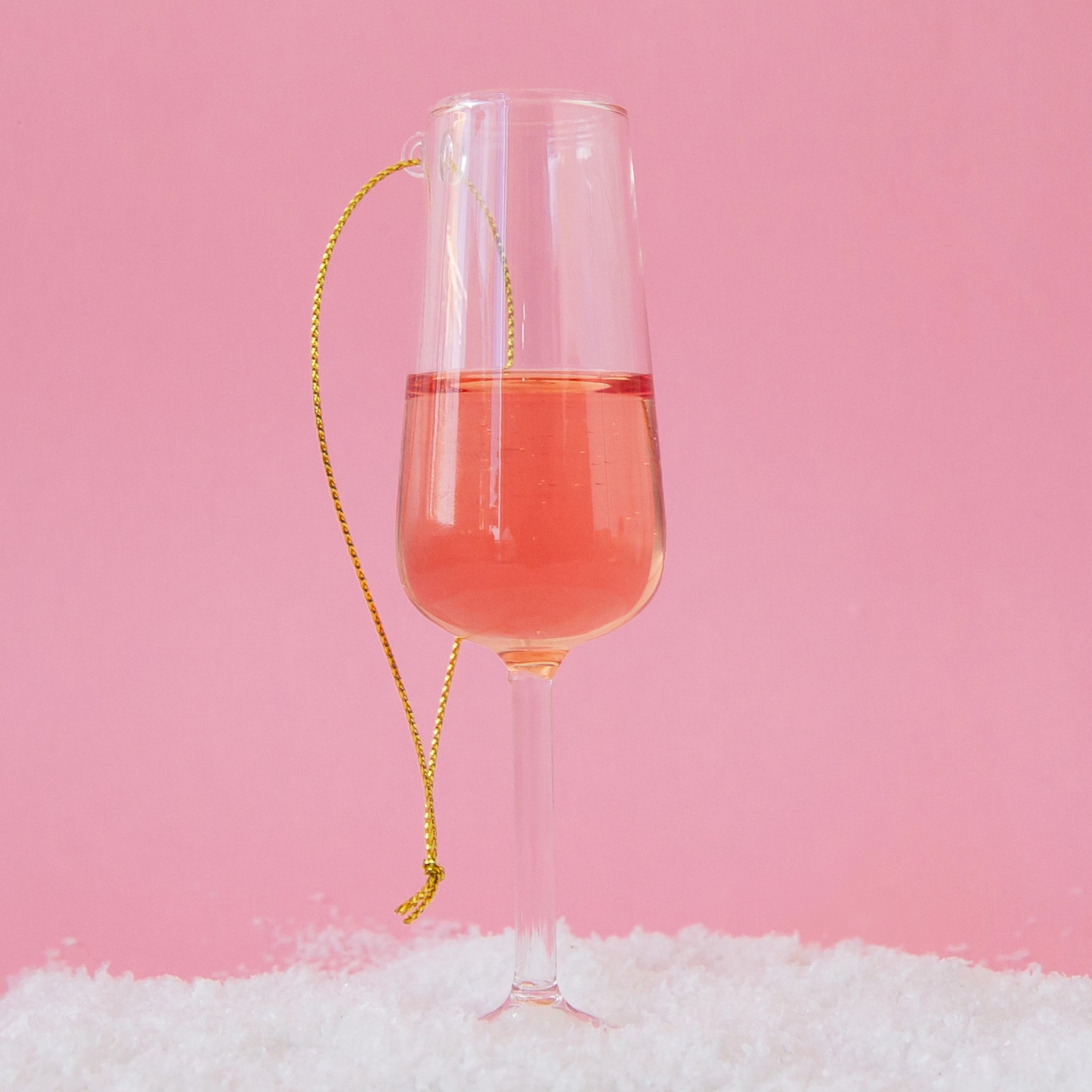 On a bright pink background is a glass ornament in the shape of a champagne flute with a pink bottom half resembling rose.