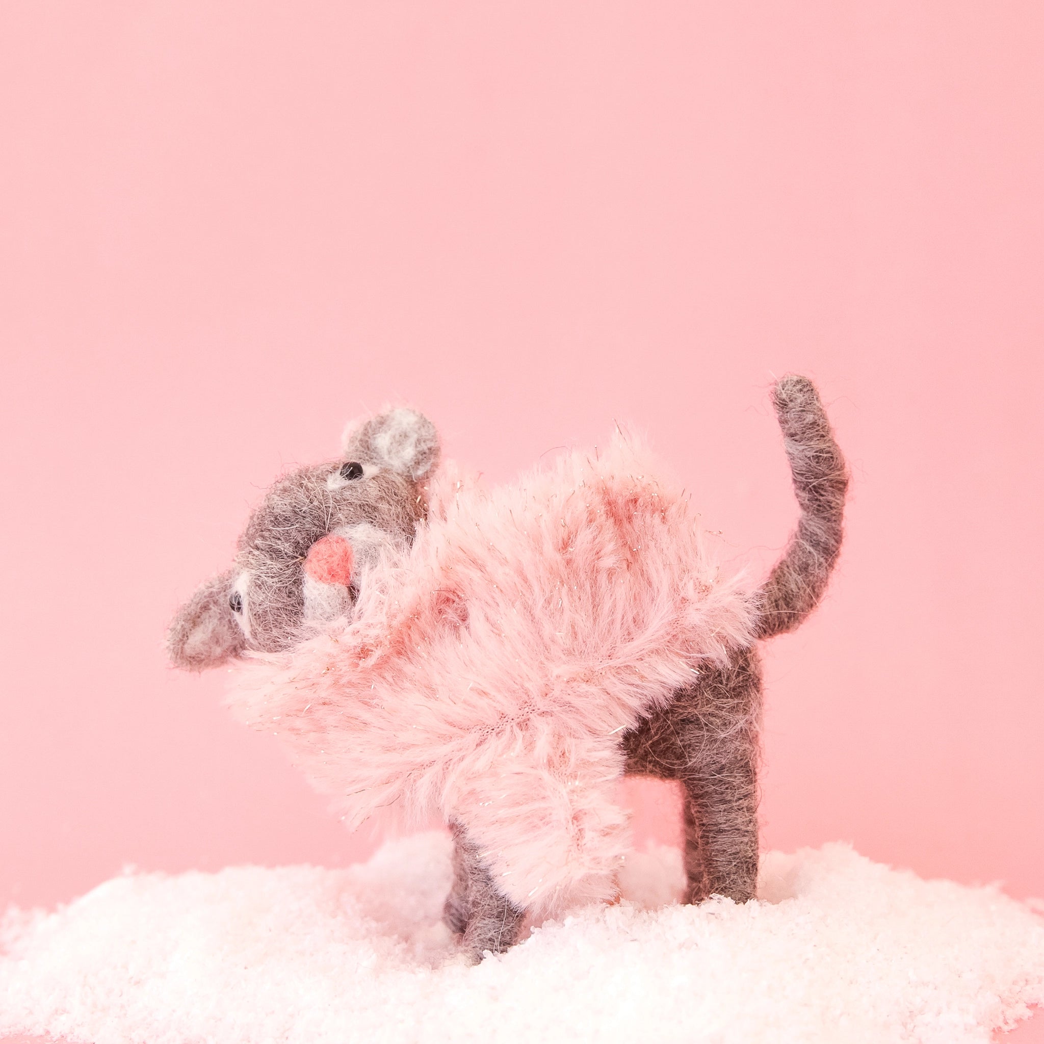 On a pink background is a brown felt cat ornament with a pink fluffy faux fur scarf. 