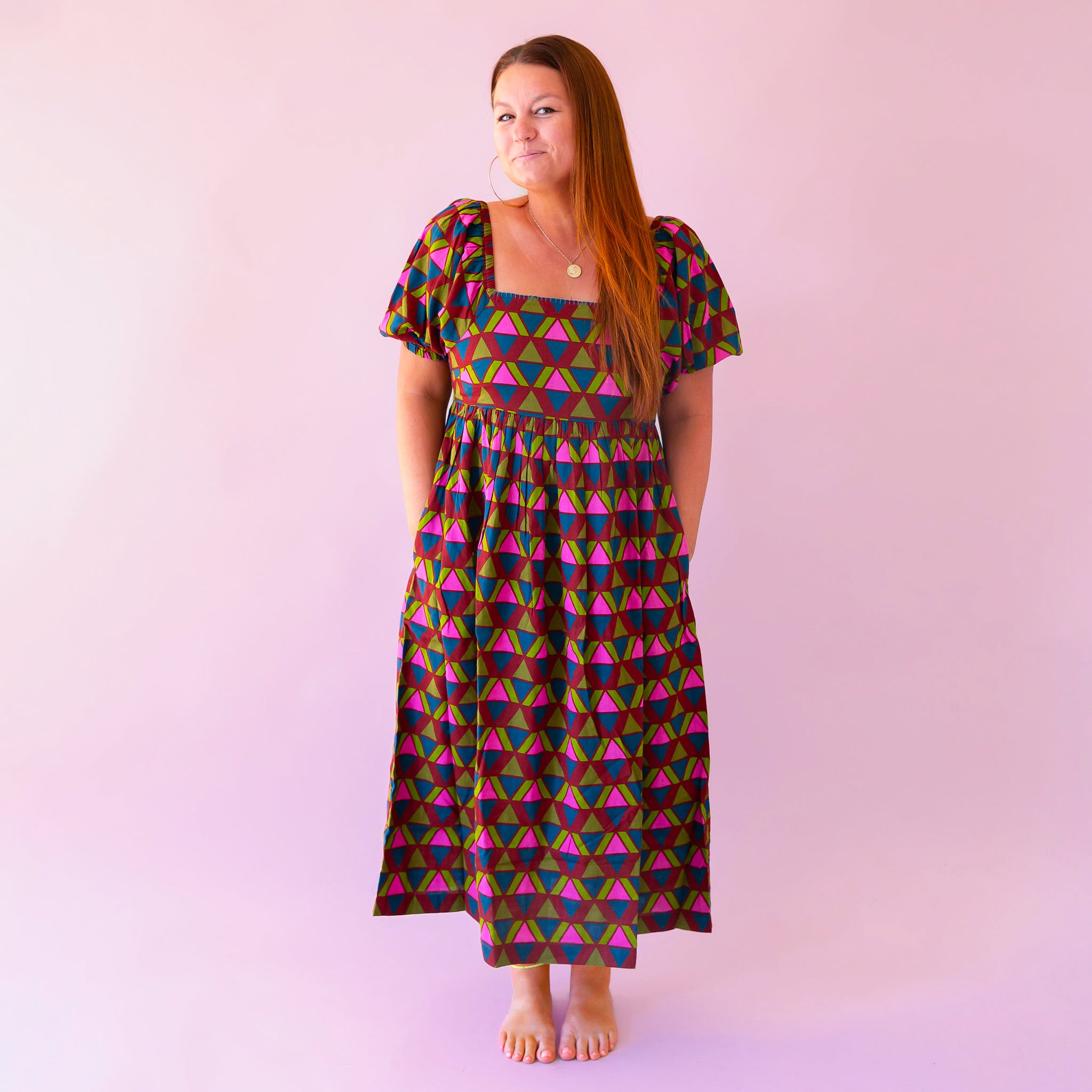 A pink, green, teal and red triangle patterned maxi dress with a square neckline, pockets and puff sleeves.