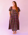 A pink, green, teal and red triangle patterned maxi dress with a square neckline, pockets and puff sleeves.