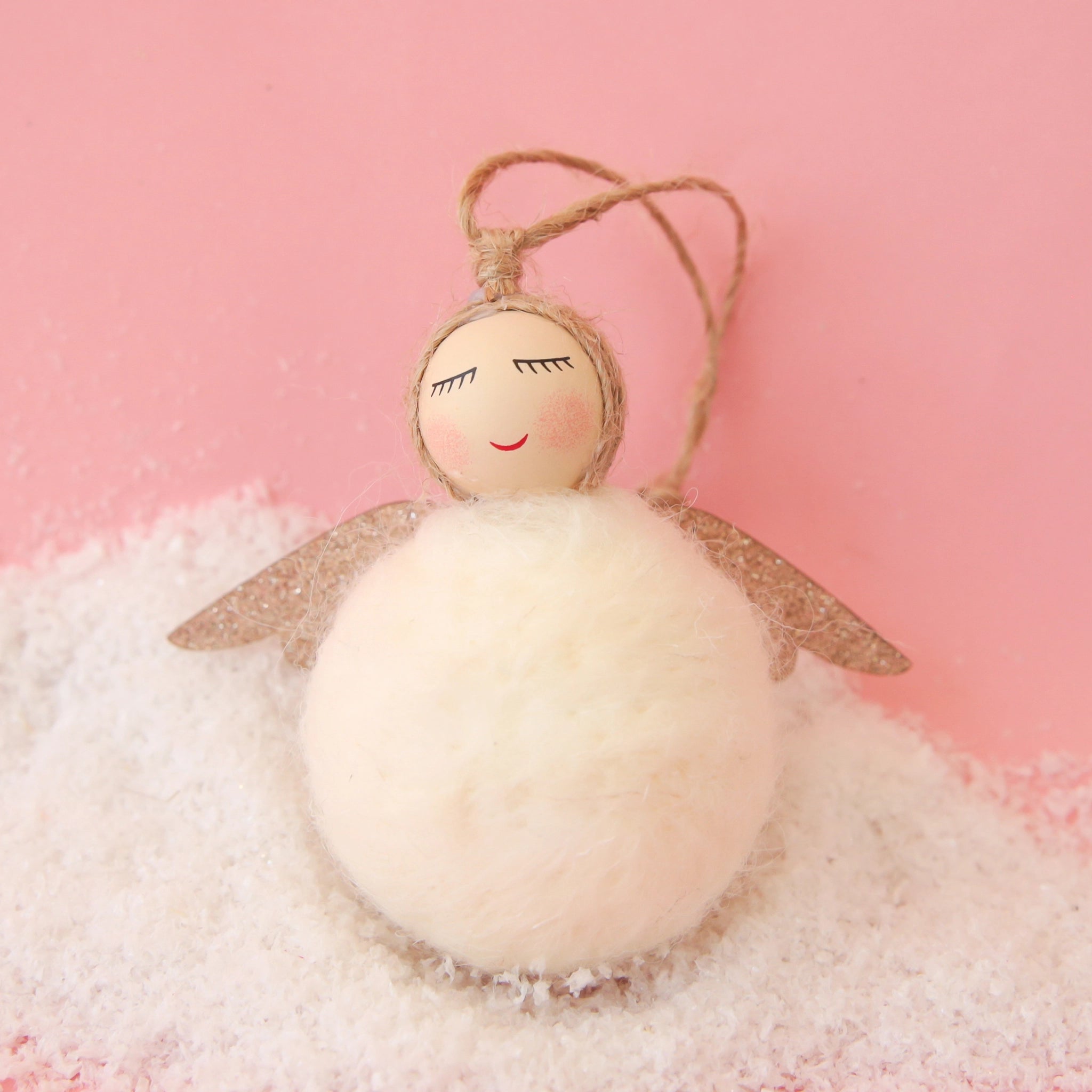 A white felt ball ornament that serves as the angels body along with a wooden bead head with a smiling face and gold sparkle wings. Also pictured is the twine loop for hanging.