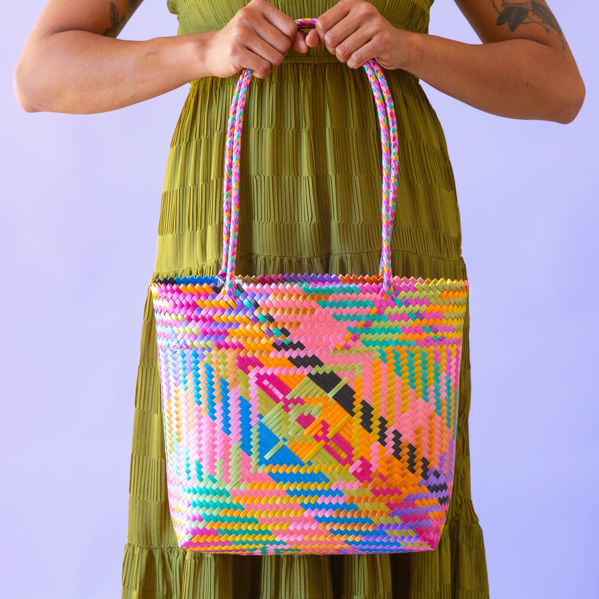 A model holding a mutli colored woven handbag with shoulder straps. 