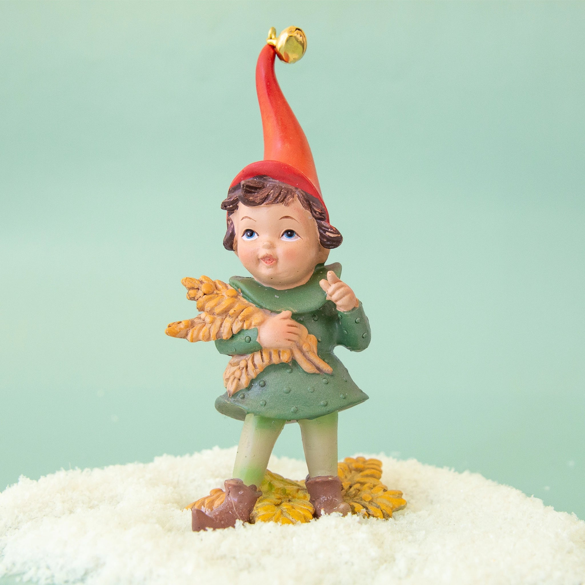 On a green background is a resin elf figurine in a green outfit and a red hat and holding grain. 