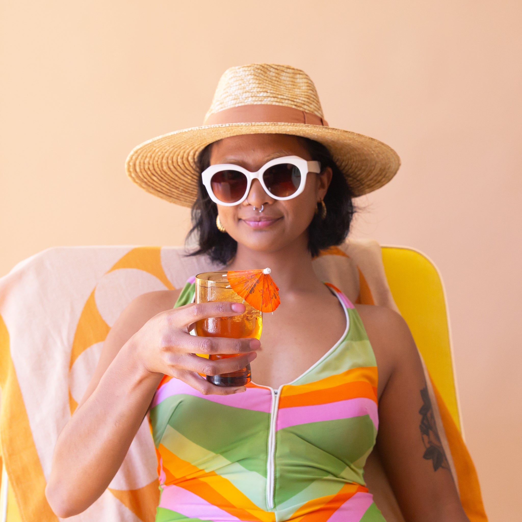 On a cream background is a model wearing a light honey colored straw sun hat with a tan ribbon around the base.