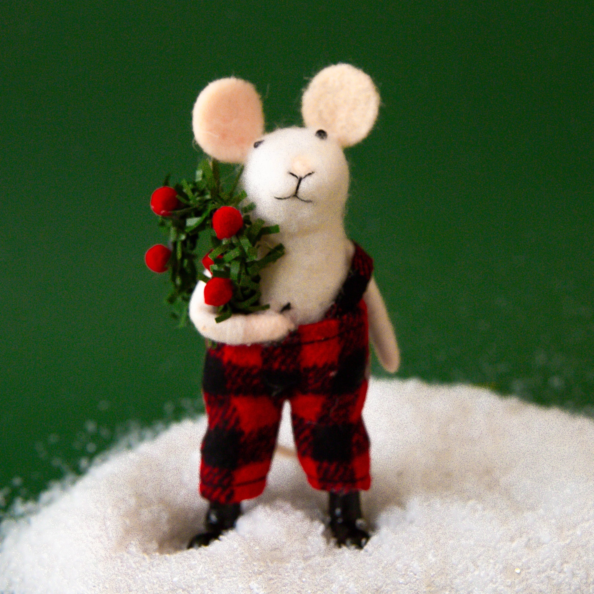 On a green background is a white mouse ornament in a black and white plaid outfit. 