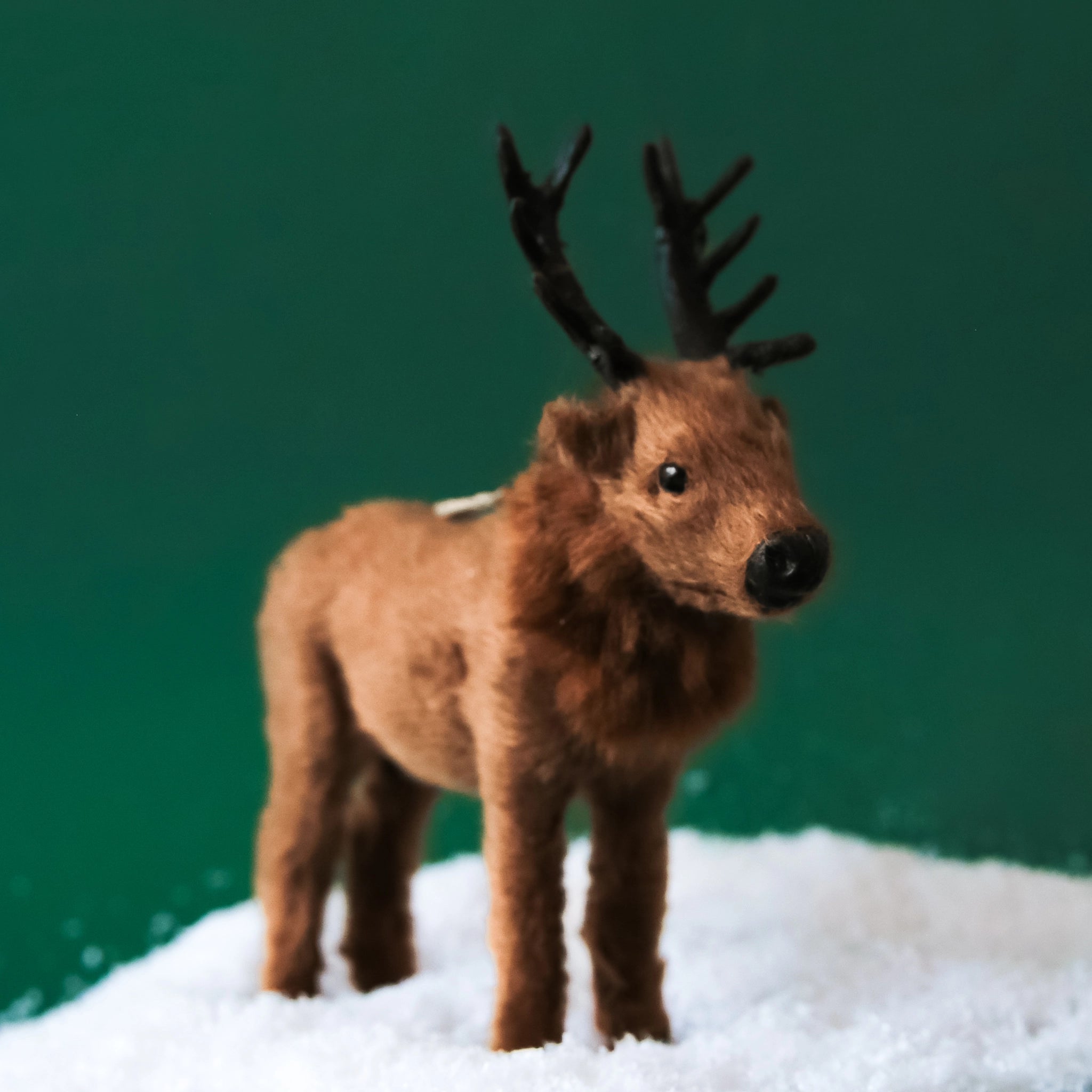 On a green background is brown furry elk shaped ornament. 