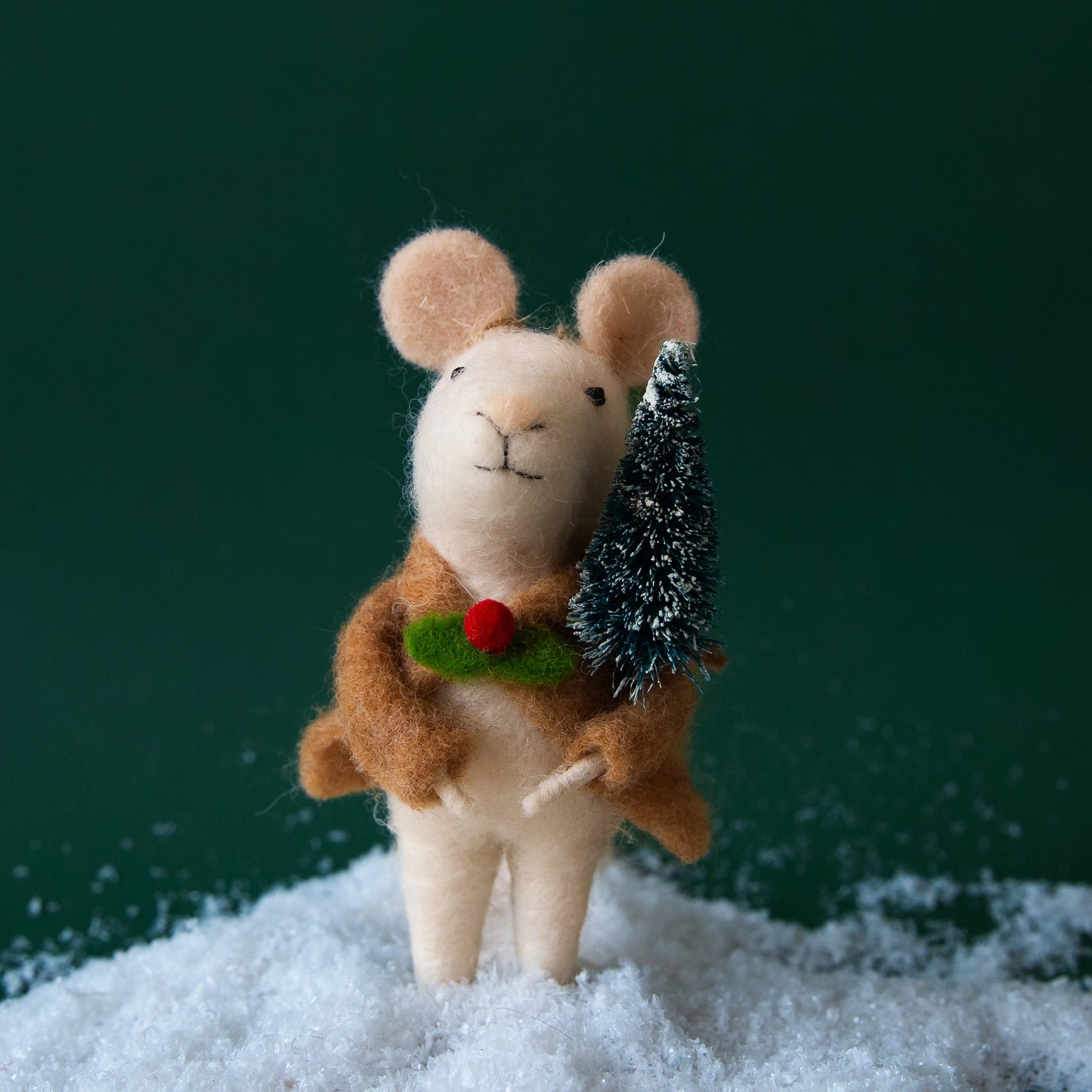 A white felt mouse ornament with a tan jacket on that has holly as the button and holding a small green bristle tree.