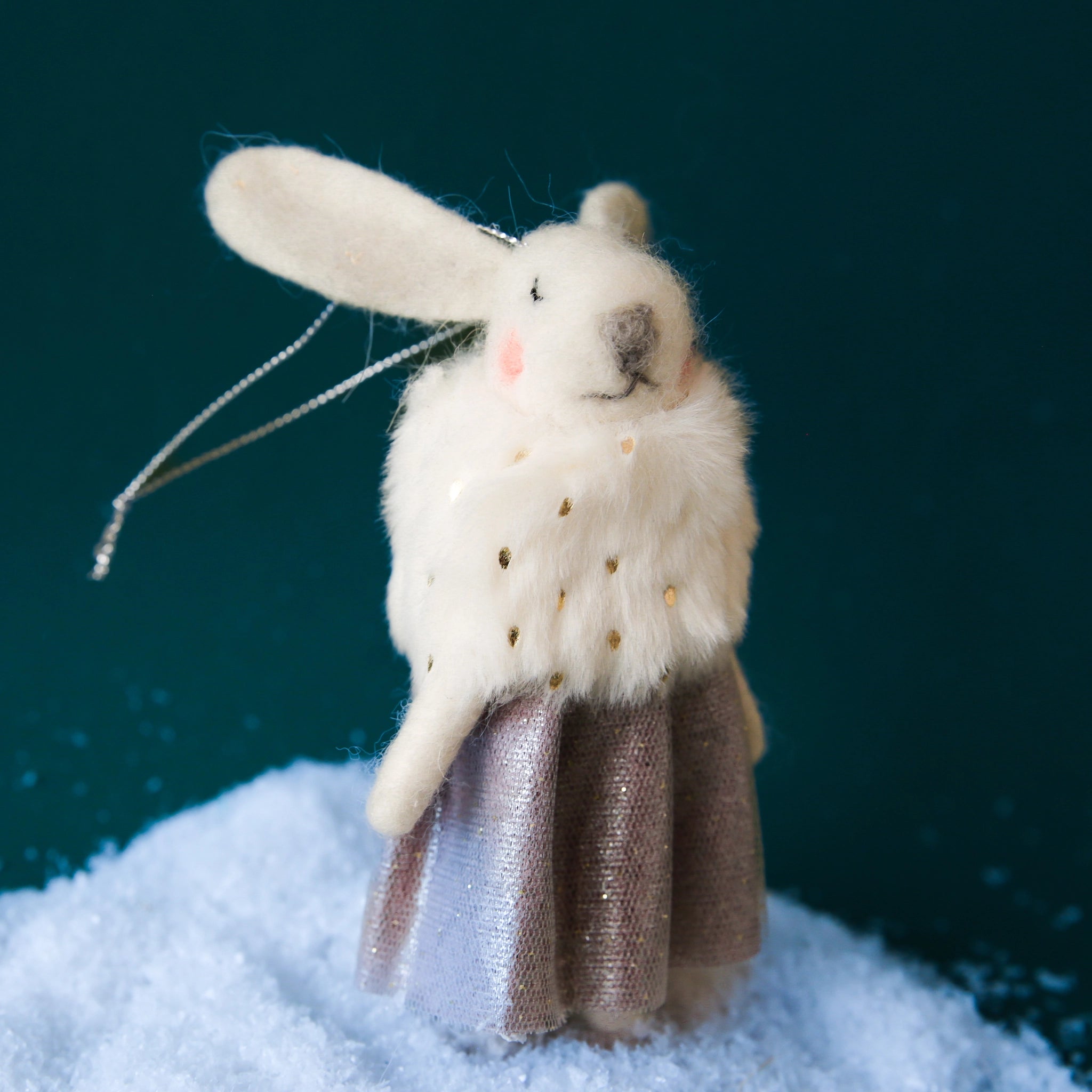 On a dark green background is a white felt bunny ornament in a fancy dress and fur scarf. 