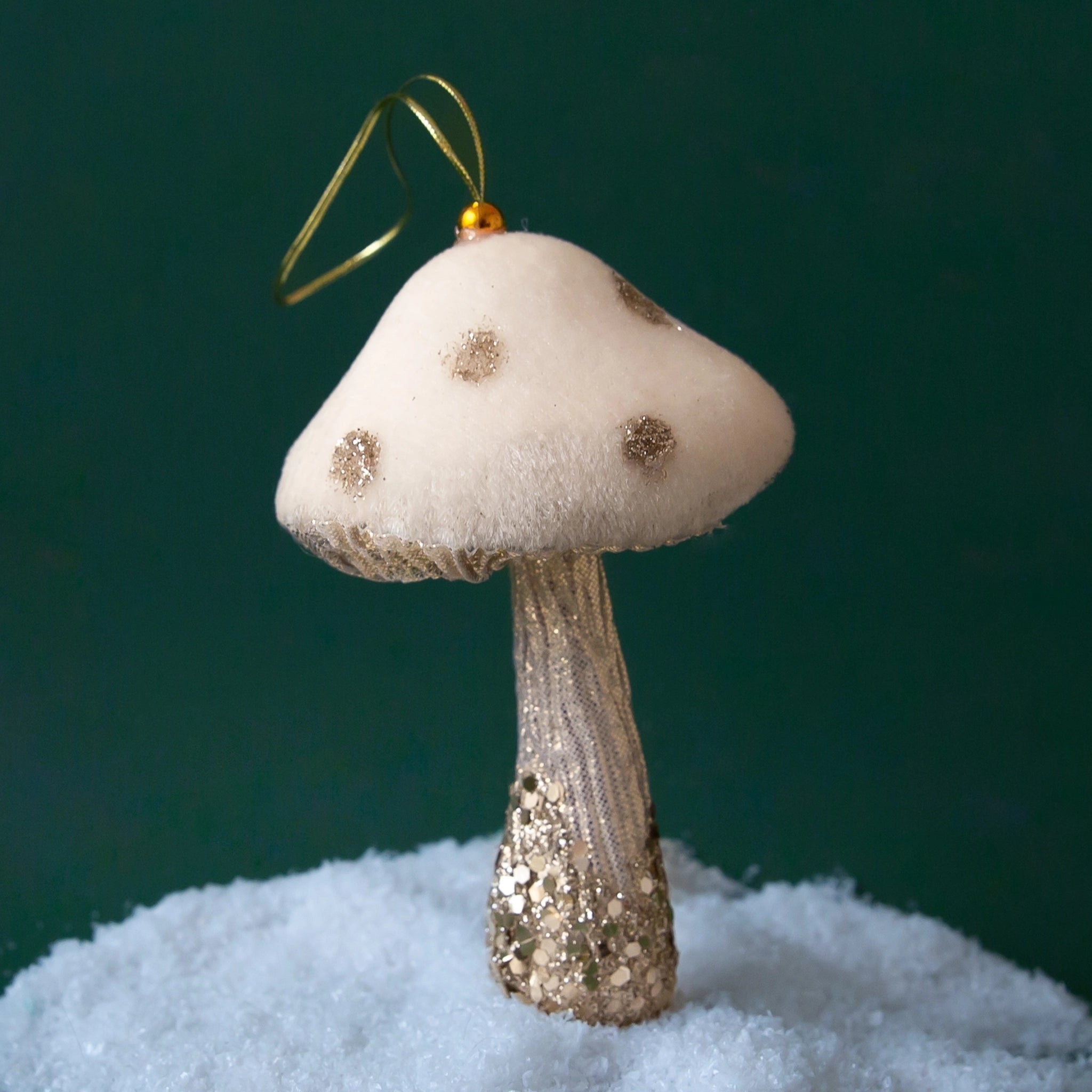 On a dark green background is a white and gold sparkle and velvet mushroom ornament.