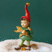 On a green background is a resin elf figurine in a green outfit and a red hat and holding grain.