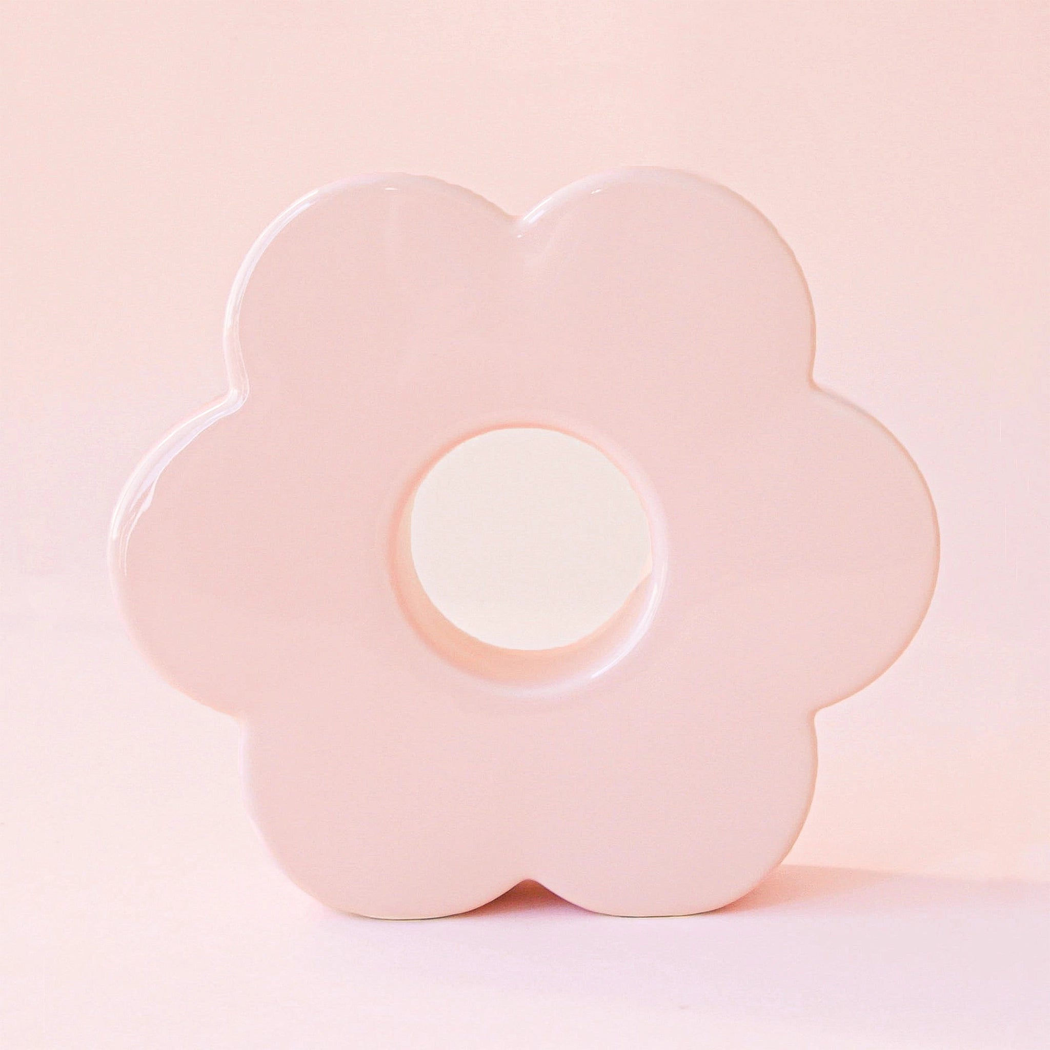 A light pink ceramic vase in the shape of a daisy with an opening in the center and an opening at the top to insert plants and floral stems.