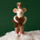 On a green background is a white felt mouse ornament with a brown outfit on and holding a gingerbread cookie. 