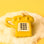 A touch tone glass phone ornament in a shiny gold color on a yellow background. 