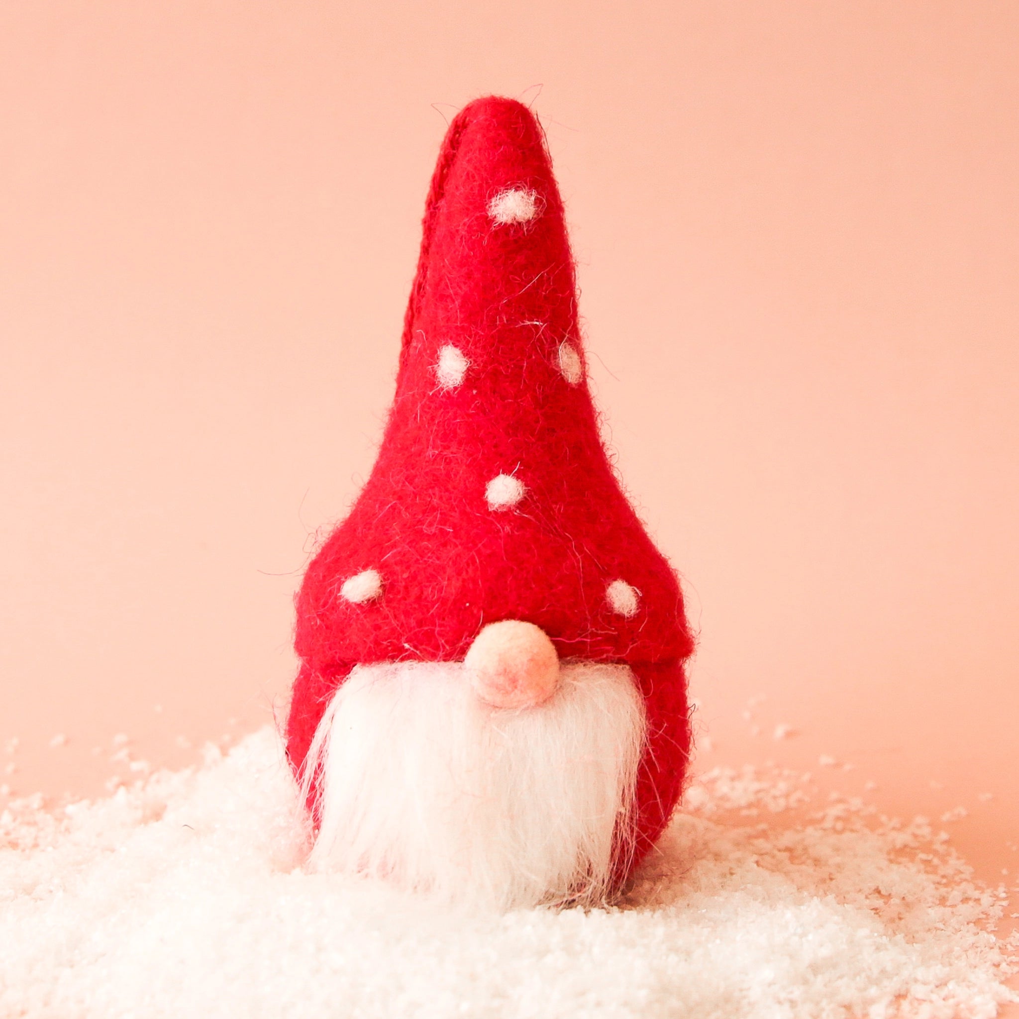 On a peachy background is a red gnome ornament with a white beard and white dots on its hat. 