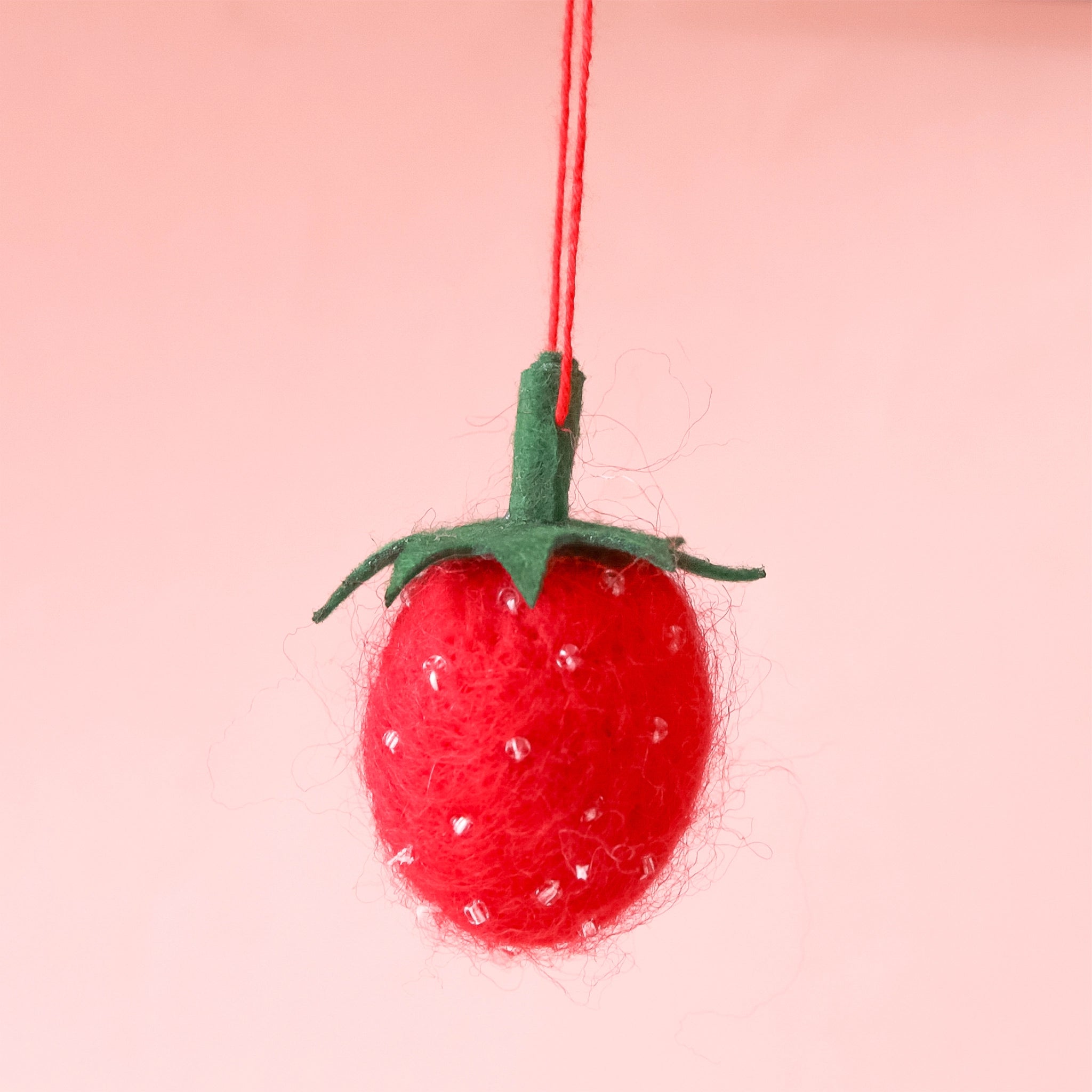 On a pink background is a felt strawberry ornament. 