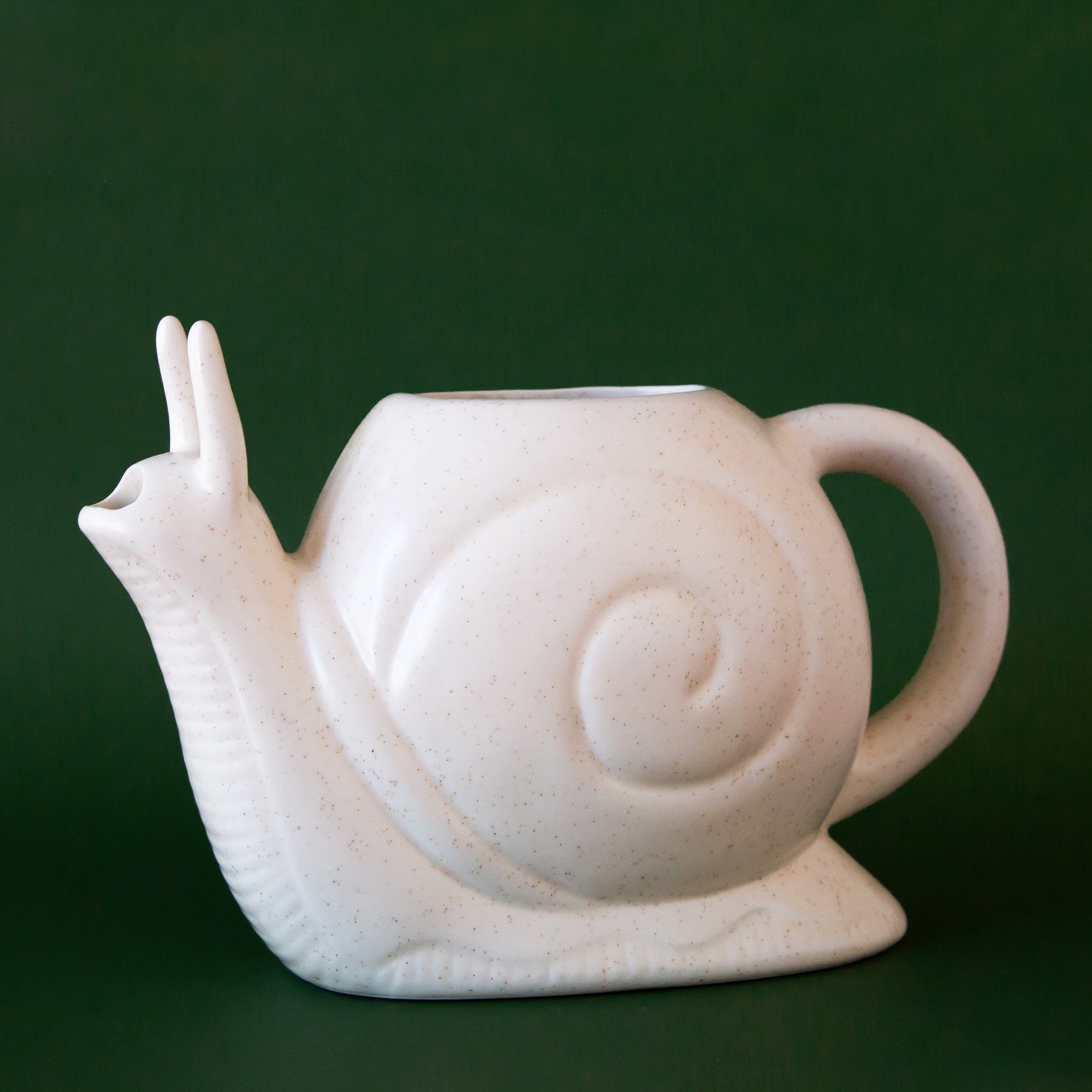 A white, ceramic watering can in the shape of a friendly snail. The opening for refilling with water is on the top of its swirly shell and the water spout comes out of the mouth area. This playful garden tool also features a comfortable handle for easy watering.