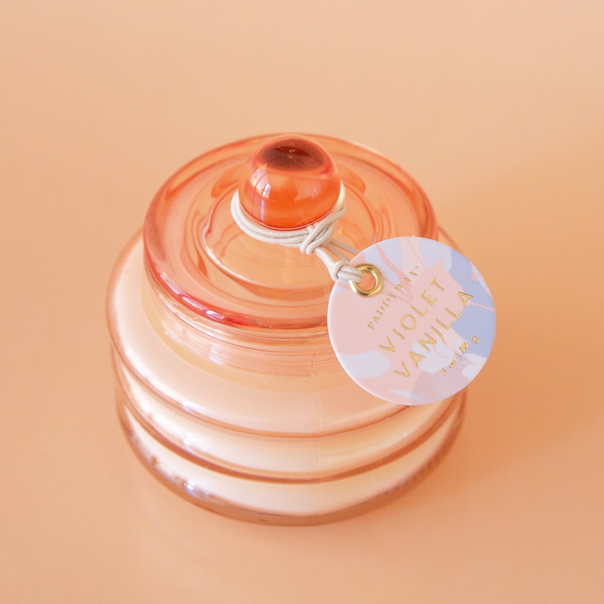 Peach colored translucent glass beam candle vessel with white wax and matching glass lid.