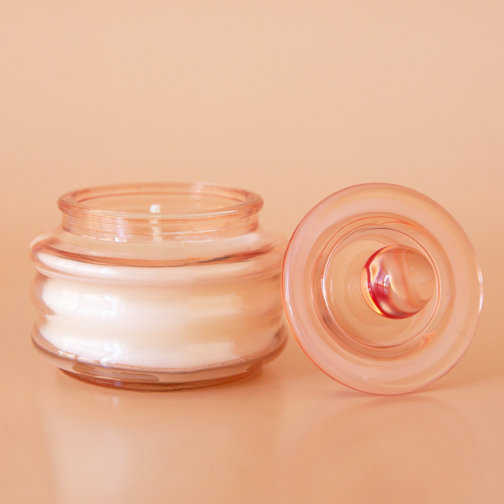 Peach colored translucent glass beam candle vessel with white wax and matching glass lid.