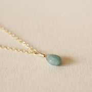 On a neutral background is a gold chain necklace with a blue Aquamarine stone at the center. 