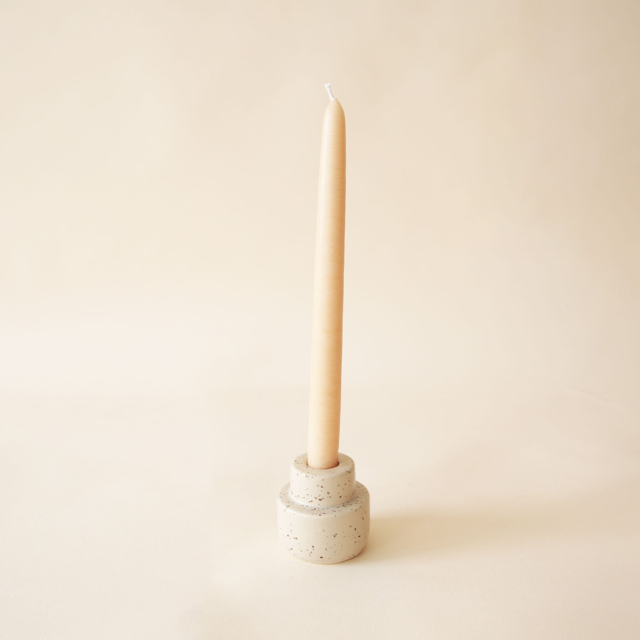 On a neutral background is an off-white ceramic candle holder with a taper candle in it that is sold separately. 