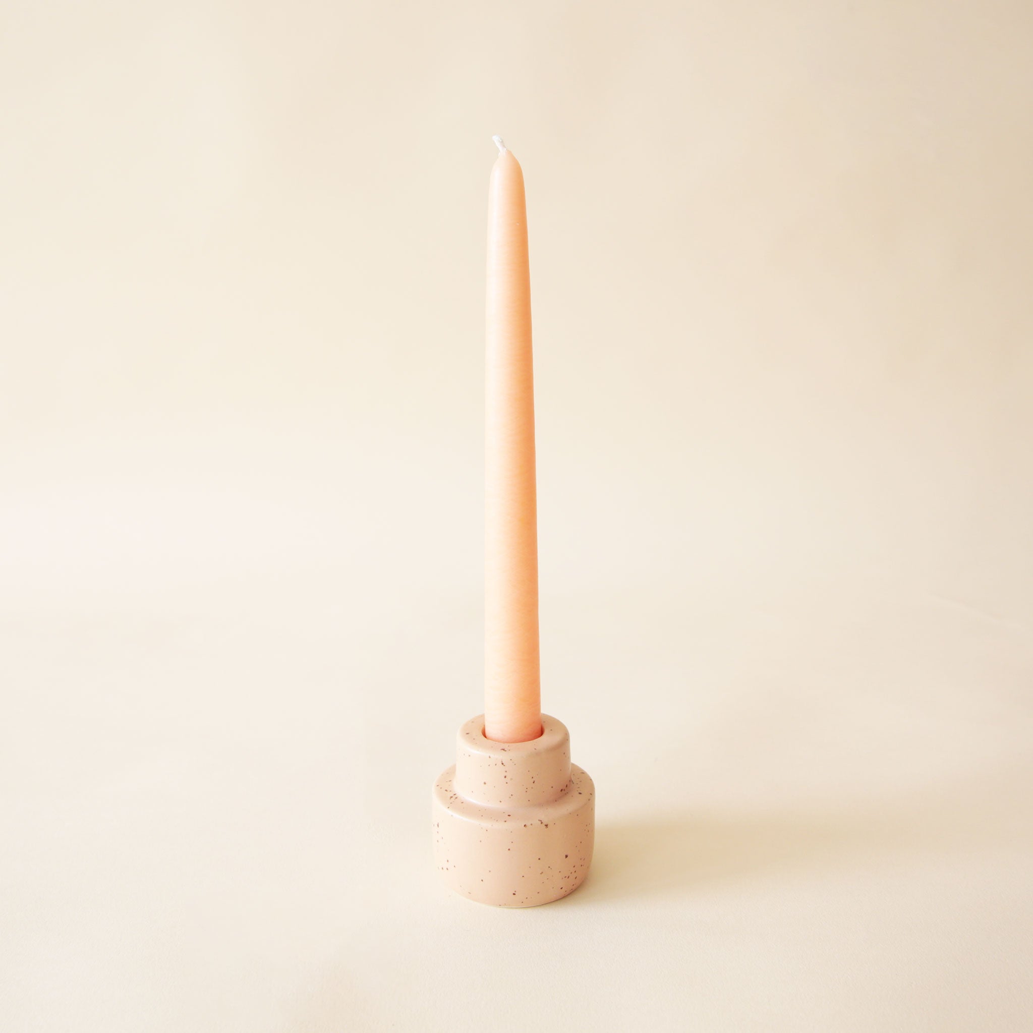 The peach colored ceramic candleholder with a taper candle in the center. 