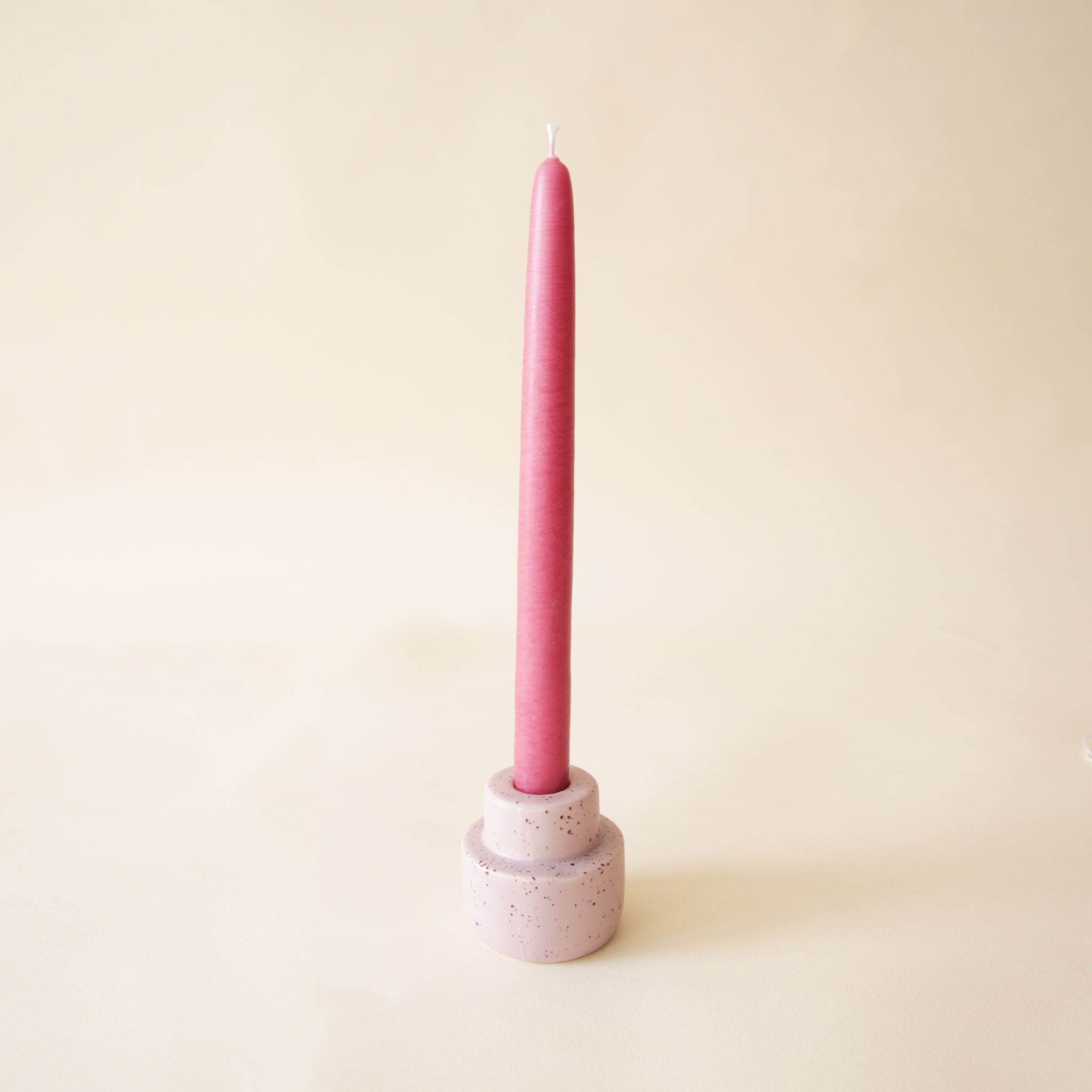 On a neutral background is a light purple ceramic candle holder with a magenta shade taper candle sold separately. 