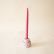 On a neutral background is a light purple ceramic candle holder with a magenta shade taper candle sold separately. 