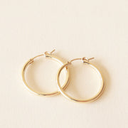 On a neutral background is a pair of thin gold hoop earrings. 