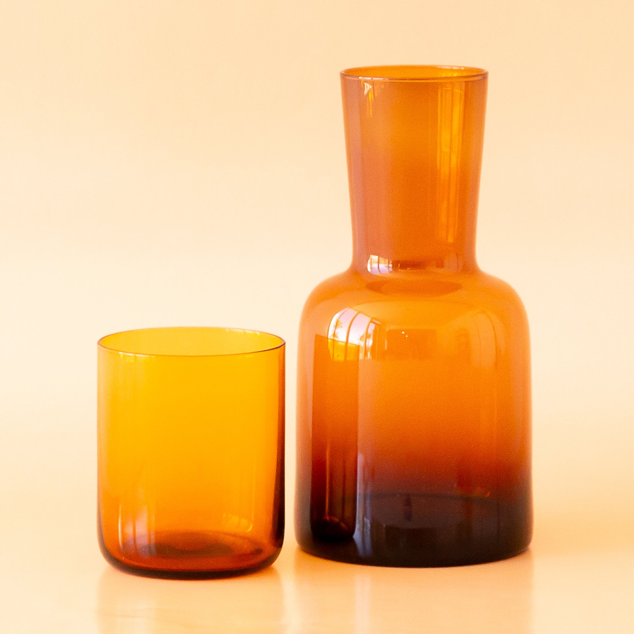 On a tan background is an amber glass carafe with a lid that doubles as a drinking glass.