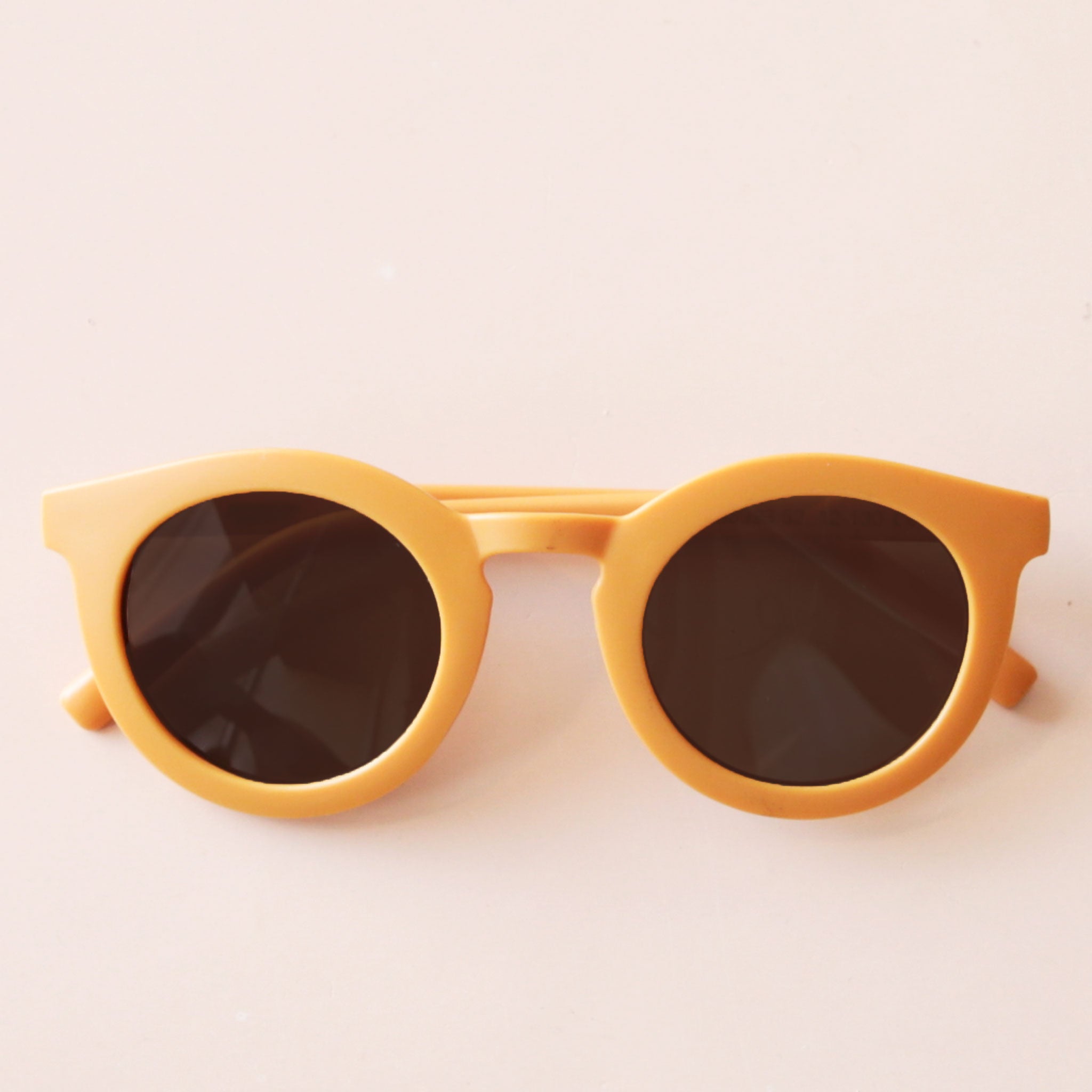 On a neutral background is a yellow pair of circle children&#39;s sunglasses. 